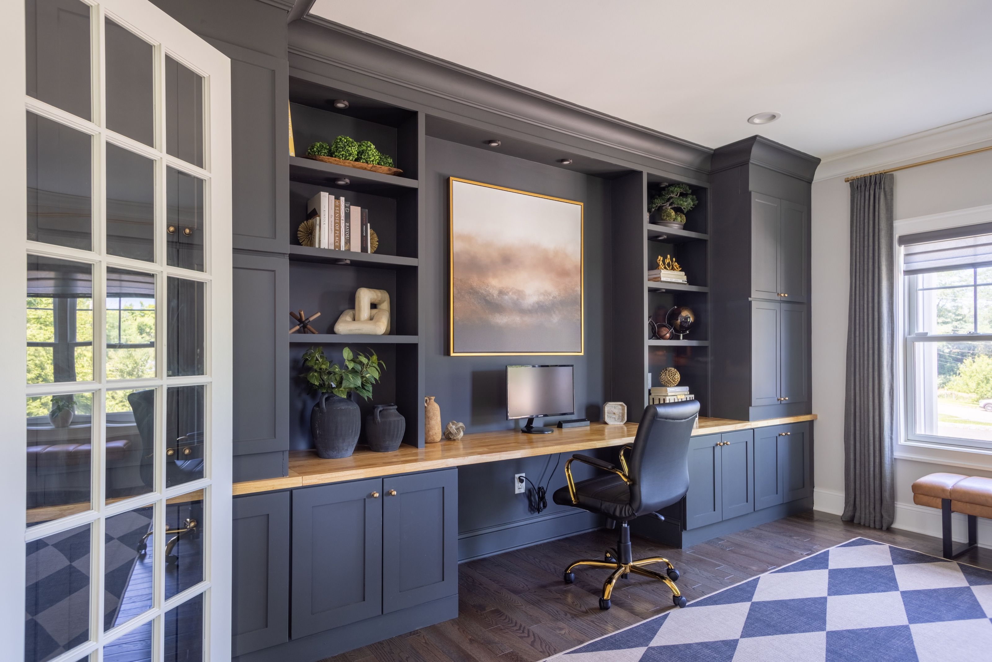 Home office with charcoal built-in shelving and cabinetry, a wood desk top, and a framed abstract painting.