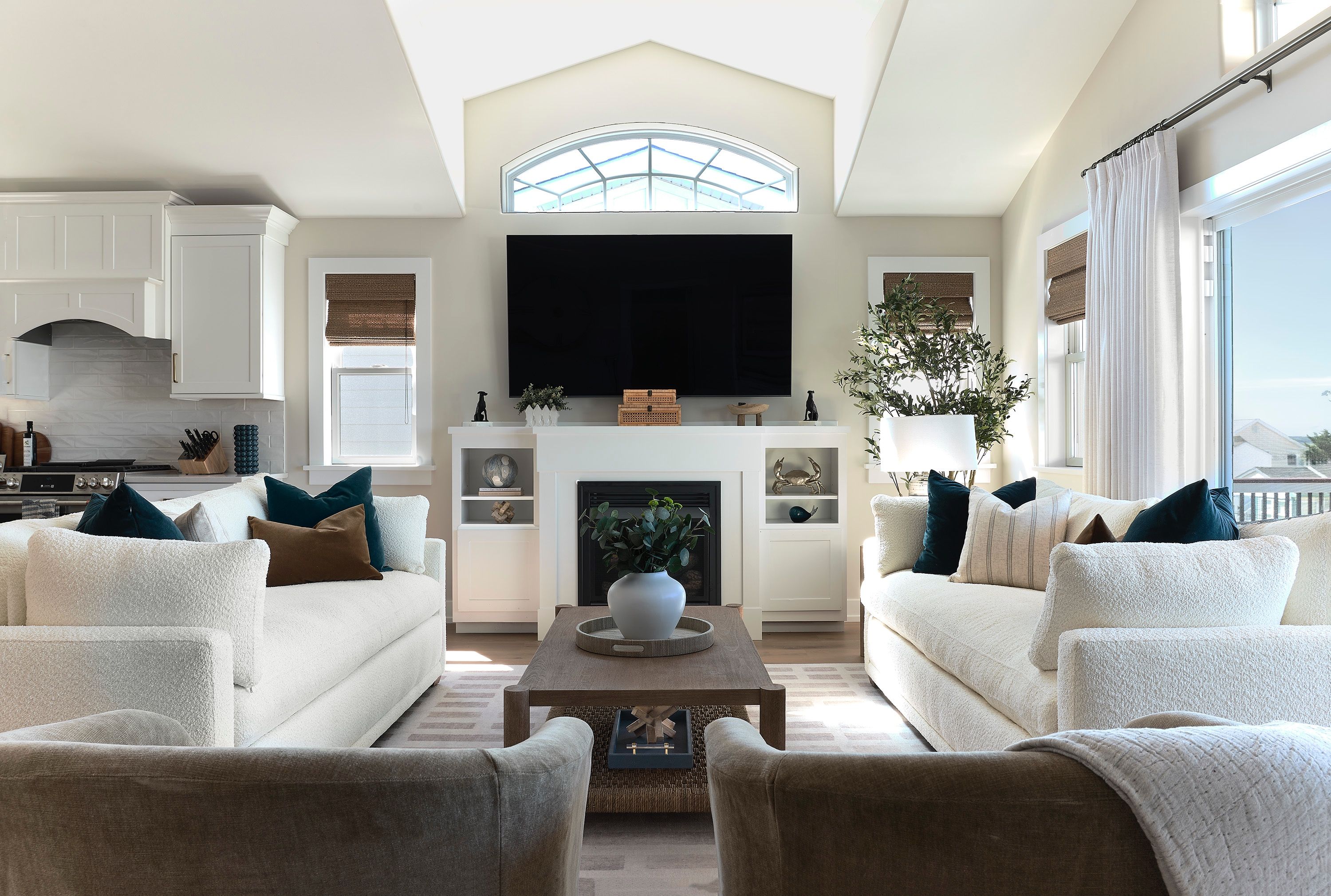 Living room with two white bouclé sofas, navy velvet pillows, and an arched window above a white fireplace built-in.
